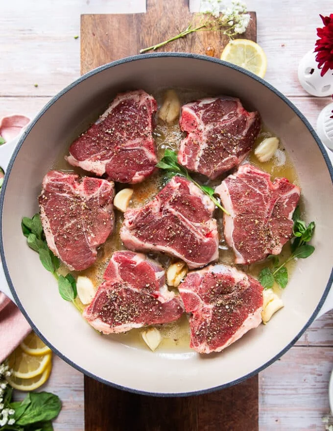 Garlic cloves and fresh herbs and lemon slices are added to the same skillet as the lamb chops for flavor