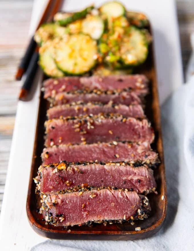A plate of seared ahi tuna, sliced up and arranged alongside some asian cucumber salad