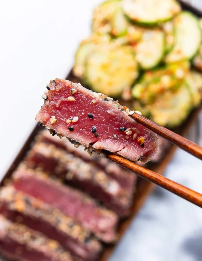 A chopstick holding a slice of seared ahi tuna up close