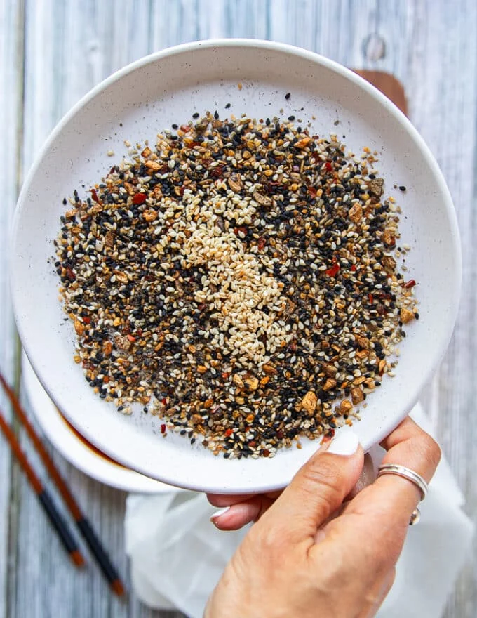 A hand holding a plate of the dried crust ingredients and mixing them together