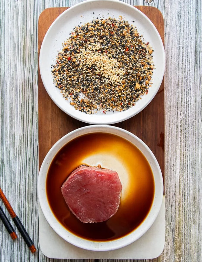 The ahi tuna fish is soaked into a plate of soy sauce as a first step to marinate the fish