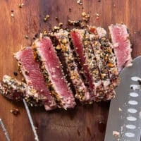 A knife slicing the ahi tuna into a 1/4th inch thick slices on a cutting board