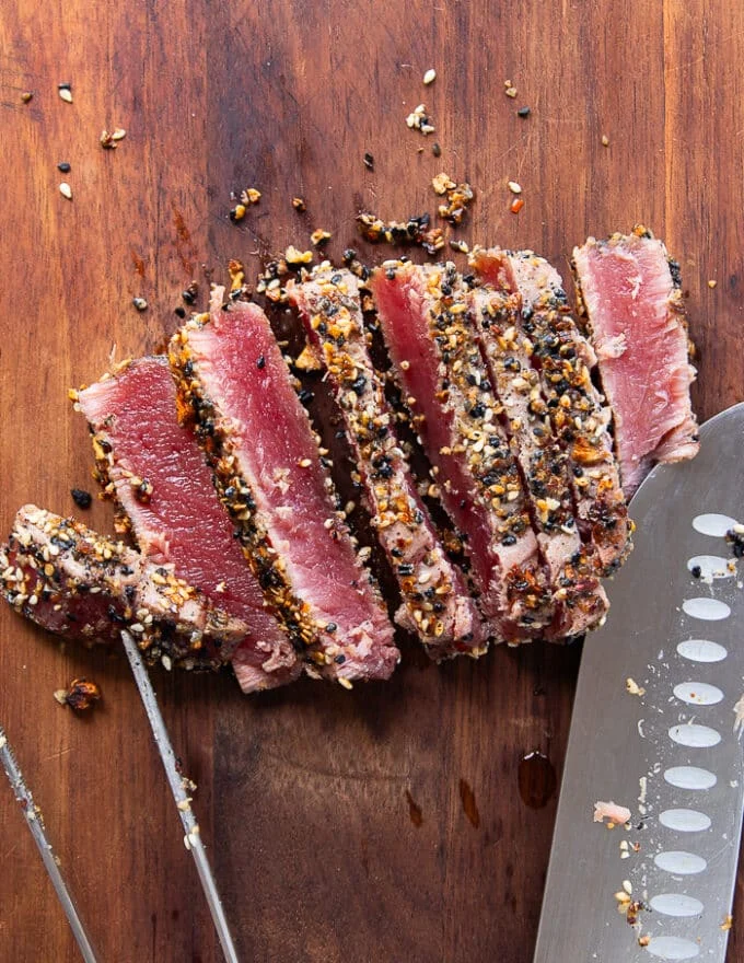 A knife slicing the ahi tuna into a 1/4th inch thick slices on a cutting board