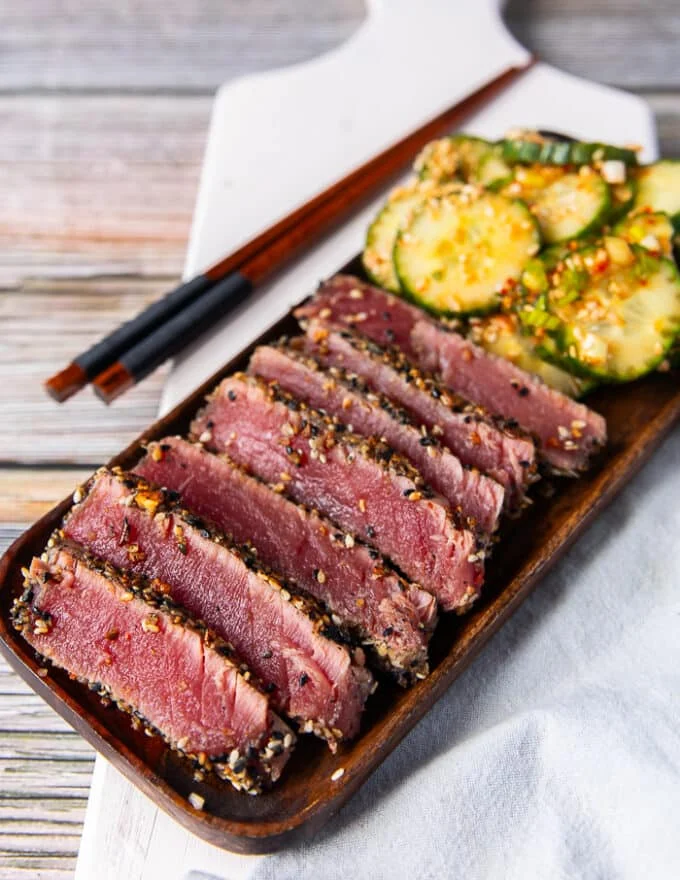 a plate of sliced seared ahi tuna recipe with some asian cucumber salad on the side