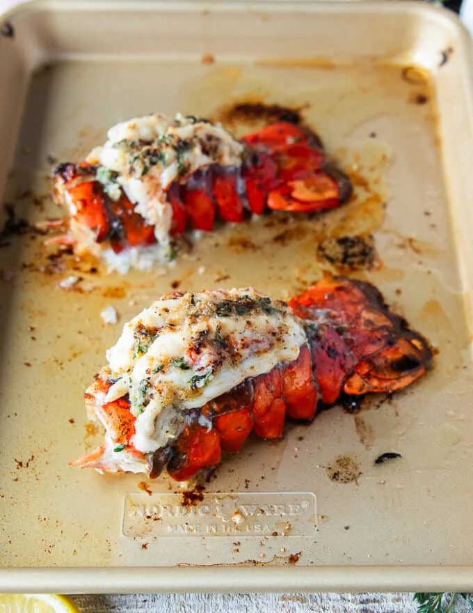 lobster tails on a baking sheet broiled and slathered in herb butter