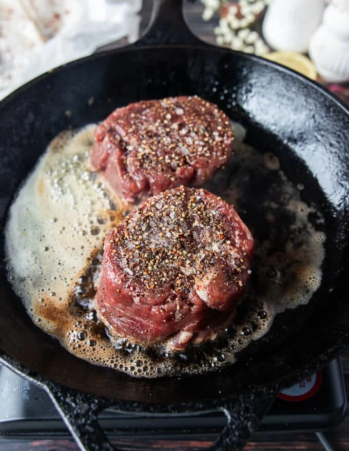 tenderloin steaks added to a cast iron skillet with butter and oil