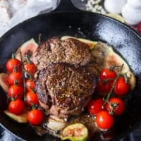 Whole garlic cloves, tomatoes on the vine and herbs are added to the cast iron skillet