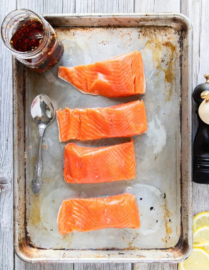 Ingredients for sweet chili salmon on a baking sheet including some salmon fillets, some chili oil, hot honey, soy sauce