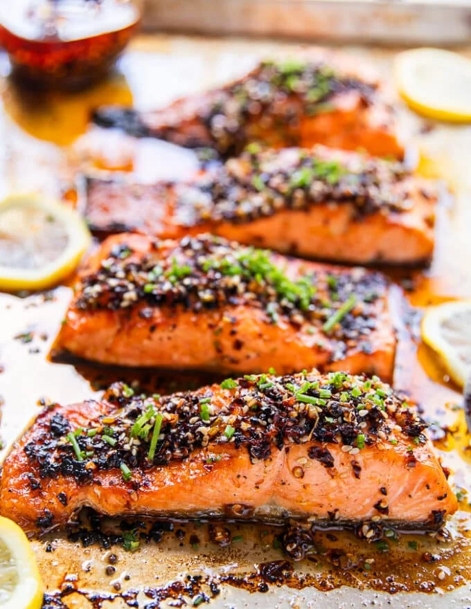 side view of salmon fillets on a baking sheet with sweet cili sauce garni9shed with green onions and surrounded by lemon slices