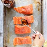 A hand spooning in the sweet chili oil sauce over the salmon
