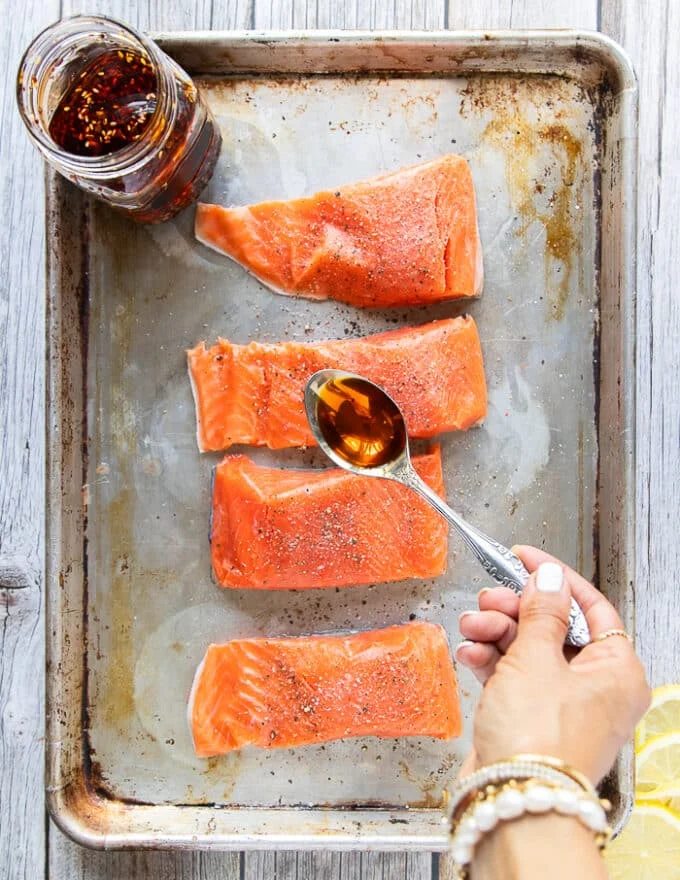 A hand spooning in the sweet chili oil sauce over the salmon