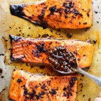 A spoon adding more sweet chili oil right over the salmon in the baking sheet once ready and out of the oven