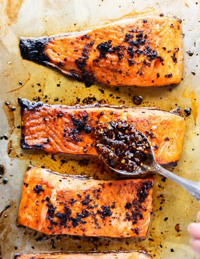 A spoon adding more sweet chili oil right over the salmon in the baking sheet once ready and out of the oven