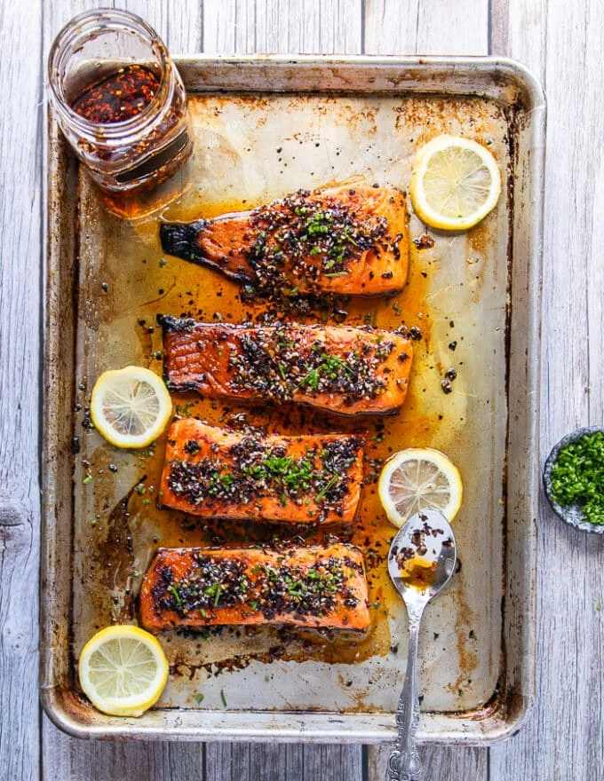 top view of a full tray of broiled salmonw ith sweet chili sauce surrounded by more chili oil and lemon slices