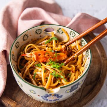 two chopsticks over a bowl of creamy chili crab pasta with a large chunk of cooked crab over the chili tossed pasta