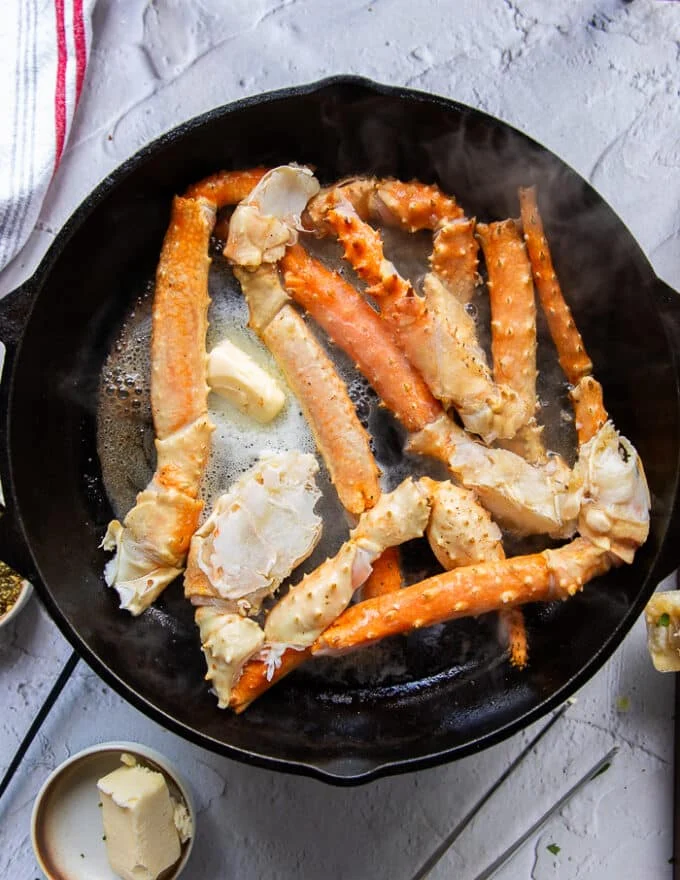 fresh crab legs cooking in a skillet with butter, salt and pepper