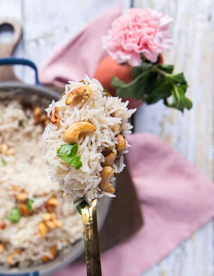 A spoon holding off some coconut rice close up showing how fluffy and well cooked it is with some toasted cashews
