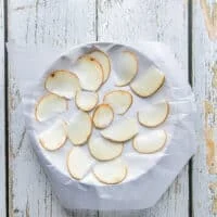 A ceramic plate with a layer of wax paper and then a single layer of potato slices spread over it