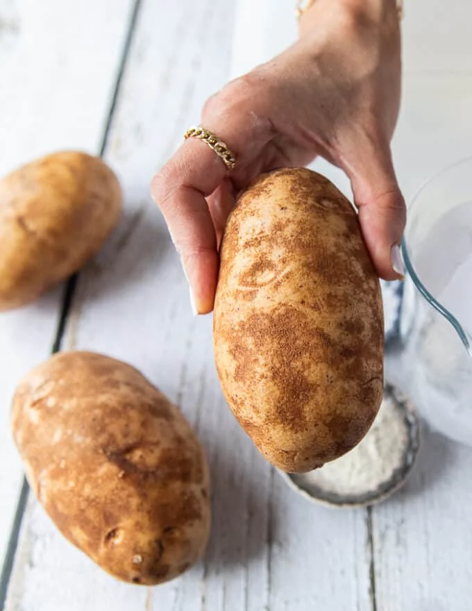 A hand holding a russet potato close up showing the best potatoes for potato chips
