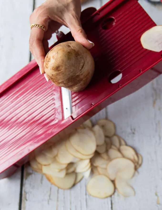 A hand slicing a russet potato using a mandolin slicer