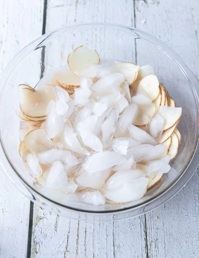 Thinly sliced potatoes in an ice bowl soaking for potato chips
