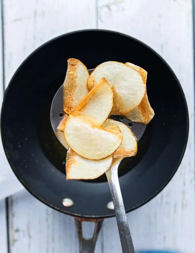 A slotted spoon slipping the chips in the hot oil