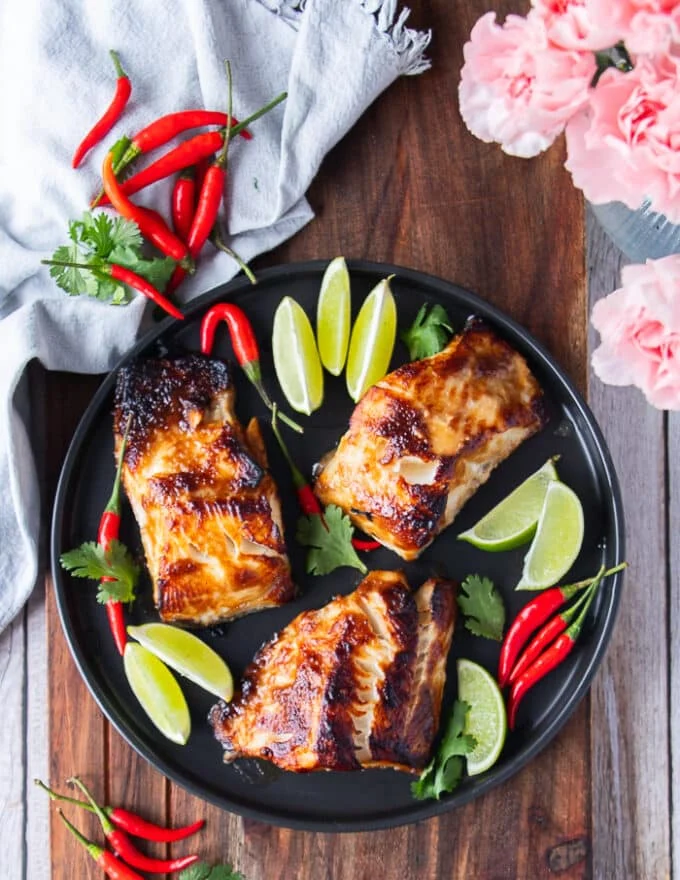 A plate of miso cod with three pieces of black cod with miso marinade, cooked until golden and surrounded with lime and red chillies