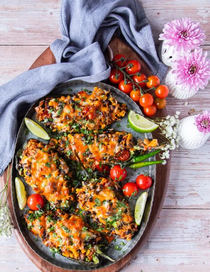 Top view of a plate of stuffed poblano peppers surrounded by lime wedges and baby tomatoes