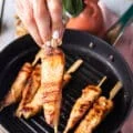 A hand holding a skewer of grilled halibut close up showing how perfectly cooked the fish is