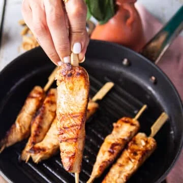 A hand holding a skewer of grilled halibut close up showing how perfectly cooked the fish is