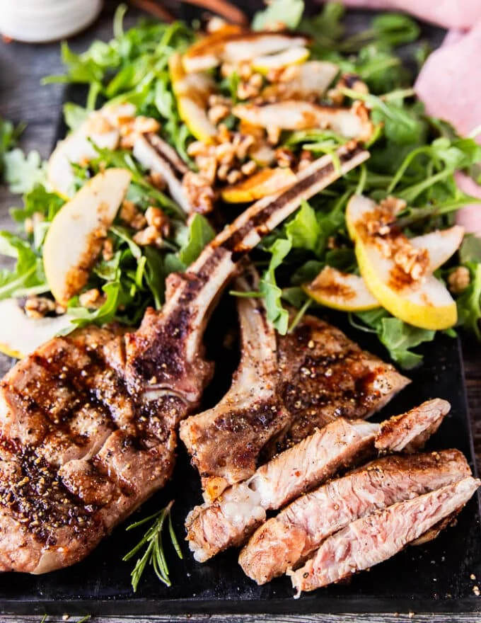 grilled veal chops on a board with one of them sliced to show how juicy it is served alongside a salad
