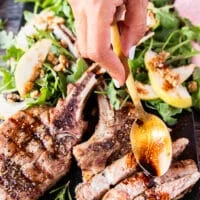 A hand using a spoon to drizzle some balsamic sauce over the grilled veal chops