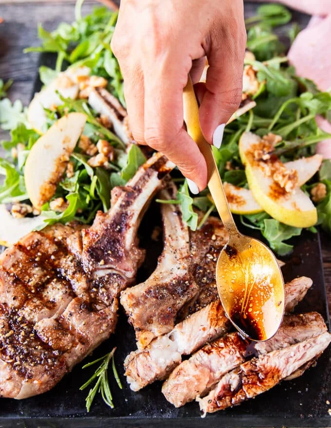 A hand using a spoon to drizzle some balsamic sauce over the grilled veal chops