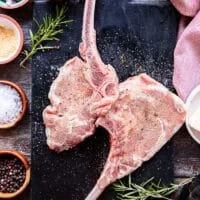 two veal chops on a marbled board seasoned on both sides with salt, pepper and granulated garlic