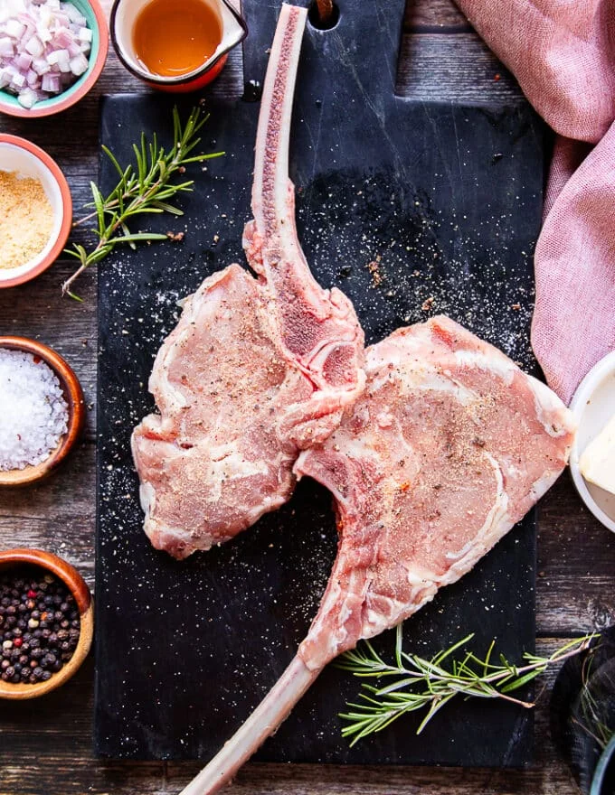 two veal chops on a marbled board seasoned on both sides with salt, pepper and granulated garlic