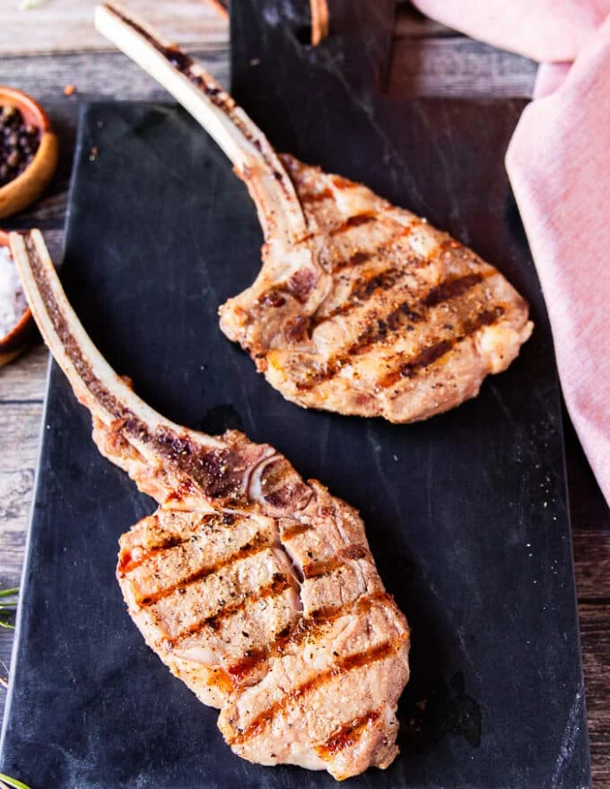 two perfectly grilled veal chops with grill marks resting on a marble after grilling