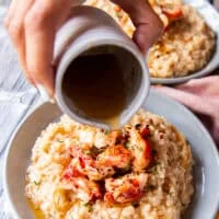 A hand drizzling the melted butter over the plated lobster risotto
