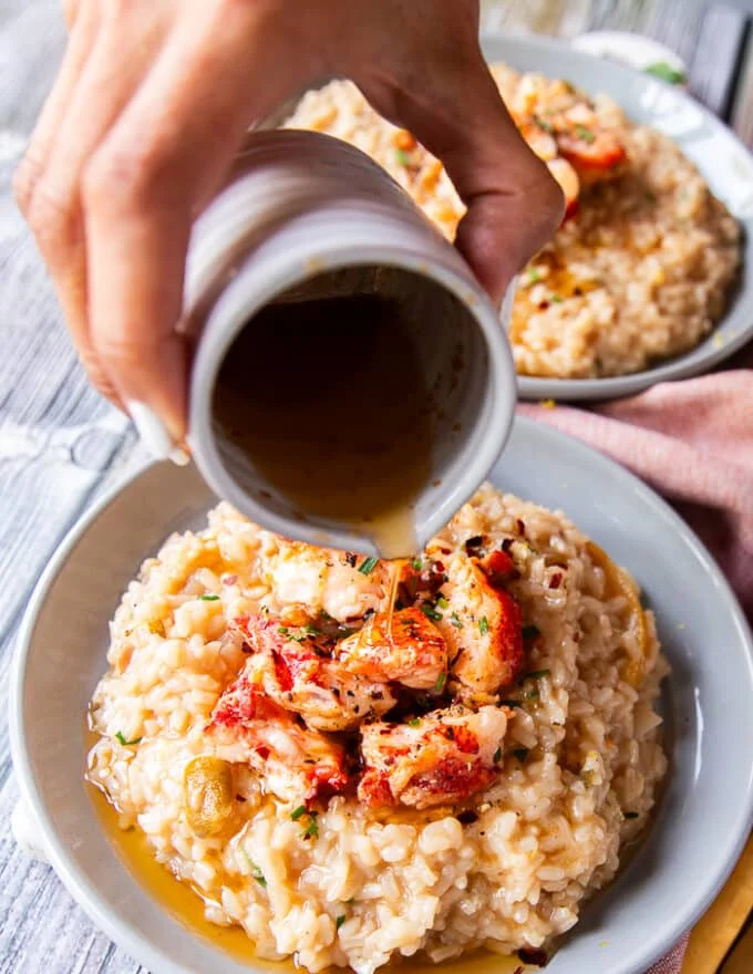A hand drizzling the melted butter over the plated lobster risotto