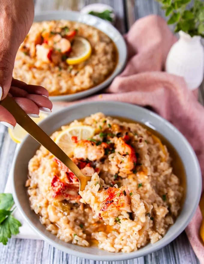 a fork scooping some lobster risotto from the plate showing the creamy texture of the risotto and buttery lobster all in one bite