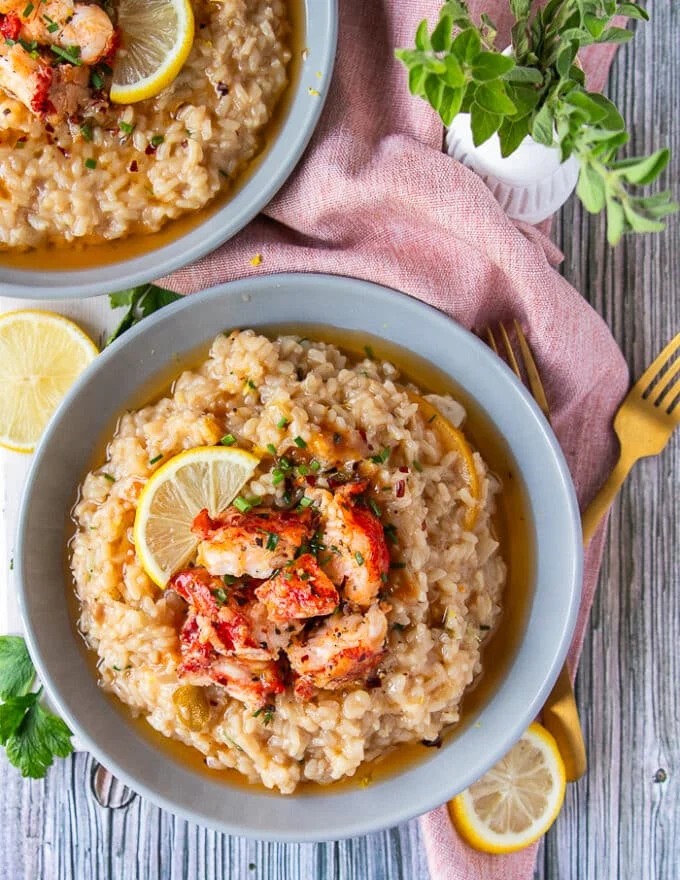 Top view of a plate of lobster risotto garnished with lemon slices and buttery cooked lobster chunks on top