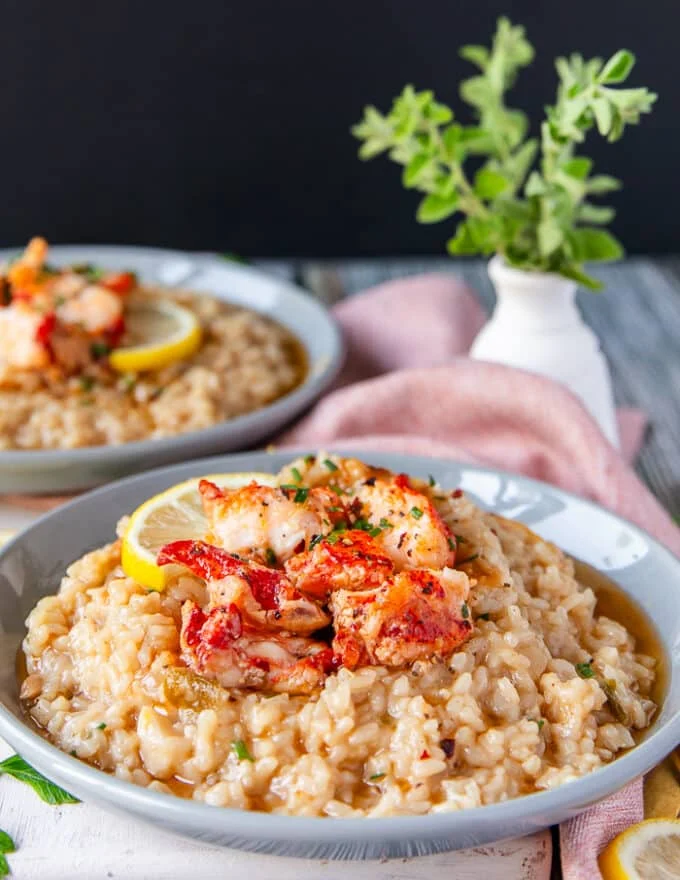 side view of two plates of lobster risotto showing the texture of the creamy risotto and buttery lobster
