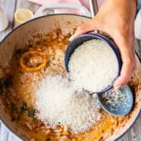 A hand pouring in the arborio rice into the skillet to make lobster risotto