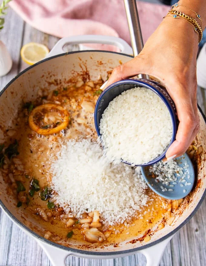 A hand pouring in the arborio rice into the skillet to make lobster risotto