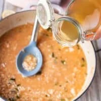 A hand pouring in more stock to the risotto skillet to continue cooking the lobster risotto