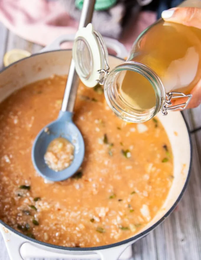 A hand pouring in more stock to the risotto skillet to continue cooking the lobster risotto