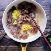 The ground beef is added to a skillet with ground ginger and garlic and a wooden spoon is mixing them