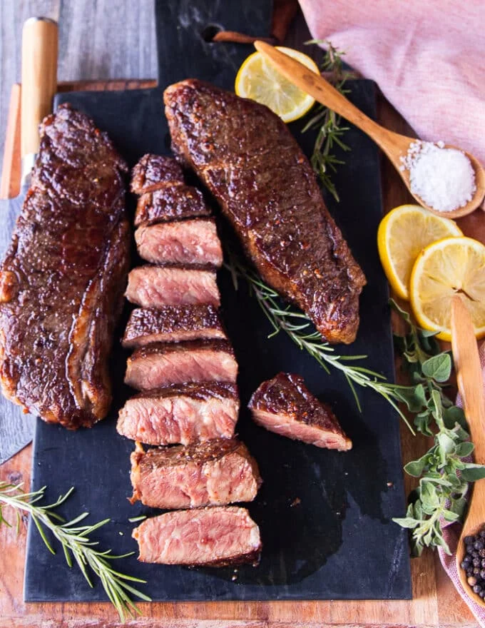 Top view of rested steak and one of them being sliced to show the golden crust and pink inside cooked to medium rare