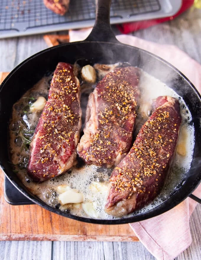 The oven cooked steaks are placed in a heavy duty cast iron pan with lots of butter for achieving the seared crust
