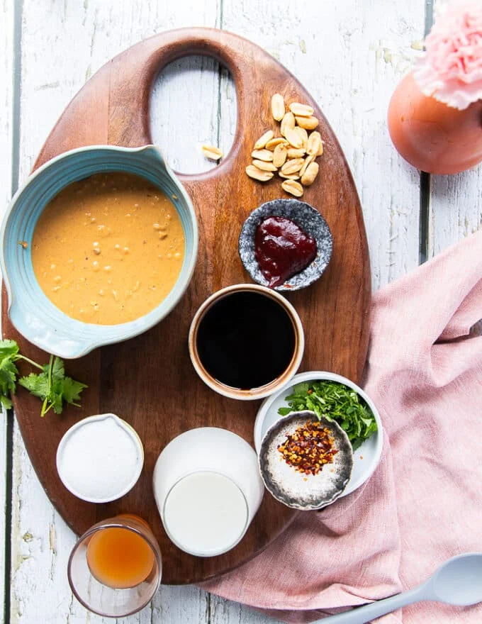 Ingredients to make satay sauce including peanut butter n a bowl, a bowl of soy sauce, a bowl of sugar a small bowl of vinegar and a cup of coconut milk