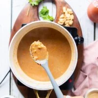 The satay sauce in a pot beginning to curdle at first and a spoon showing how it looks curdled first and that this is normal initially